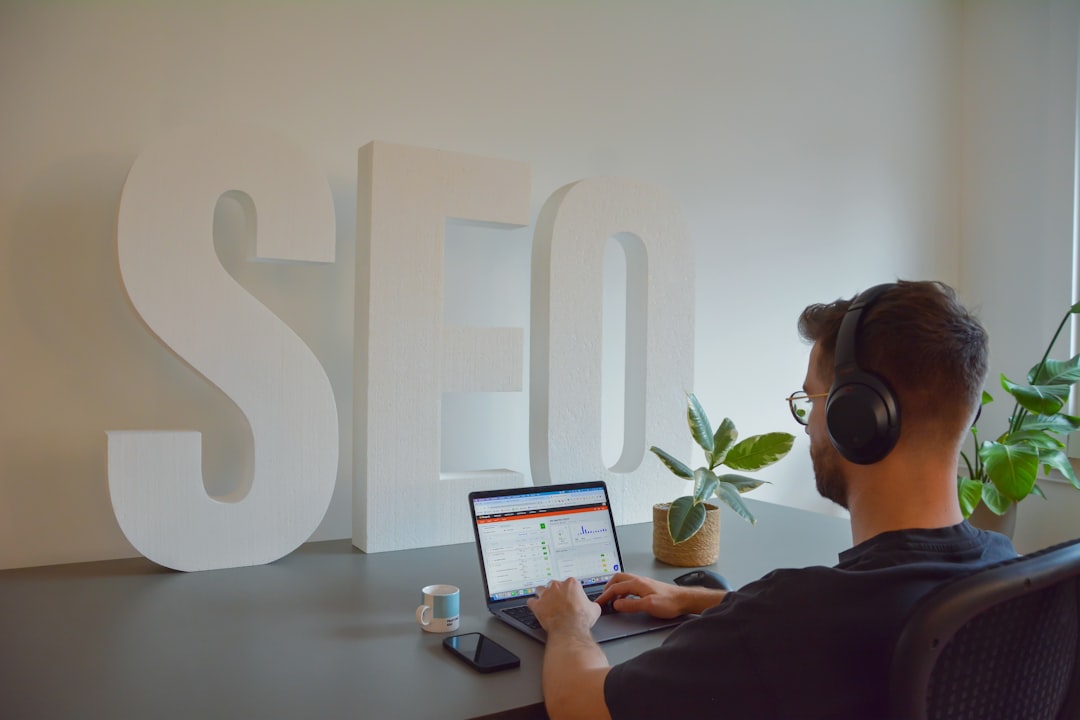 services-04 Focused professional working at an SEO agency, seated at a modern office desk. He is wearing headphones to stay concentrated, with large SEO letters in the background emphasizing the digital environment. On the desk, there is a cup of espresso, a mobile phone, and a small plant, adding a touch of greenery to the workspace.