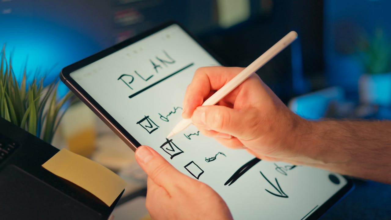 home-img Person using a digital tablet and stylus to plan and organize tasks in an office setting.
